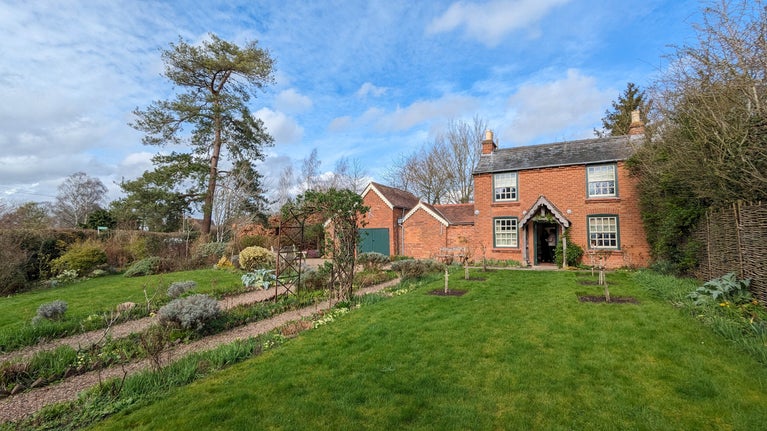 A view of Elgar's quaint redbrick birthplace cottage and cottage garden in the spring time, with primroses and hellebore's growing in the garden on a sunny spring day.